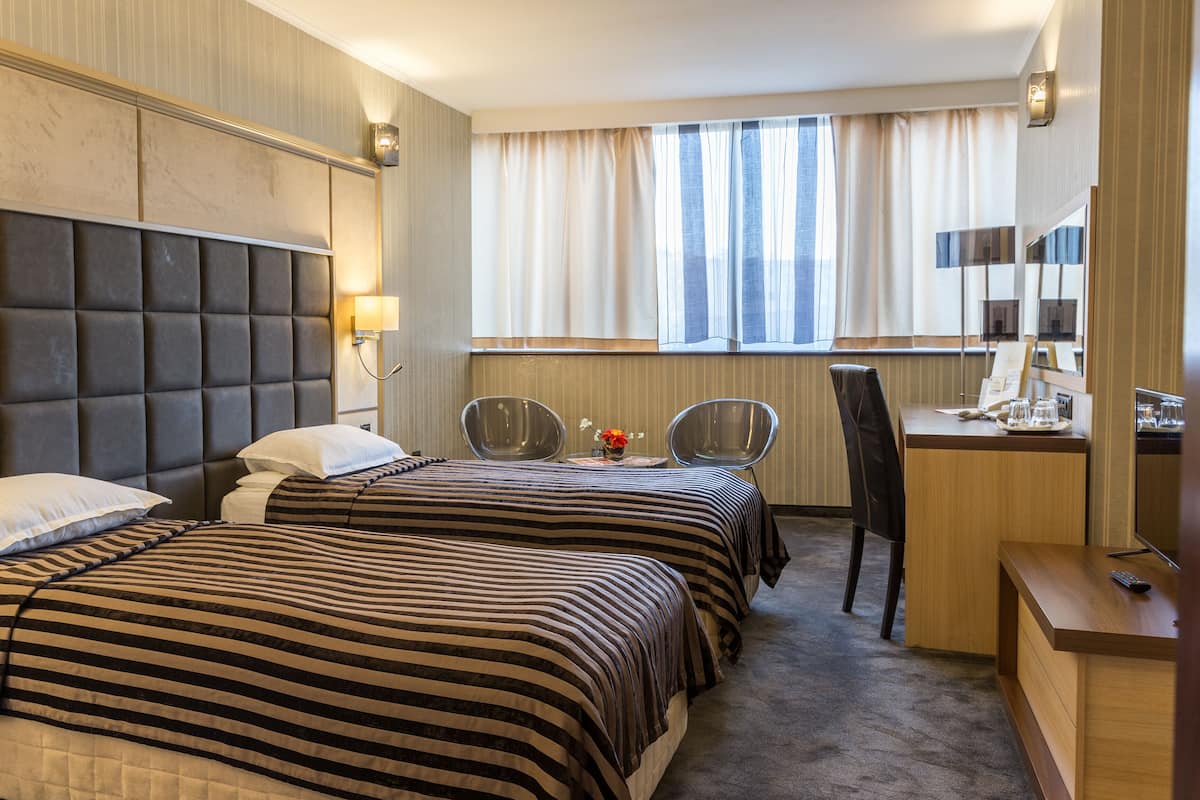 A hotel room with two beds, a desk, and a chair.