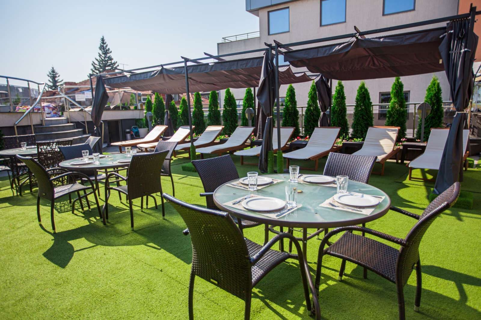 An outdoor patio with round tables and chairs, some under umbrellas, and a green artificial turf.