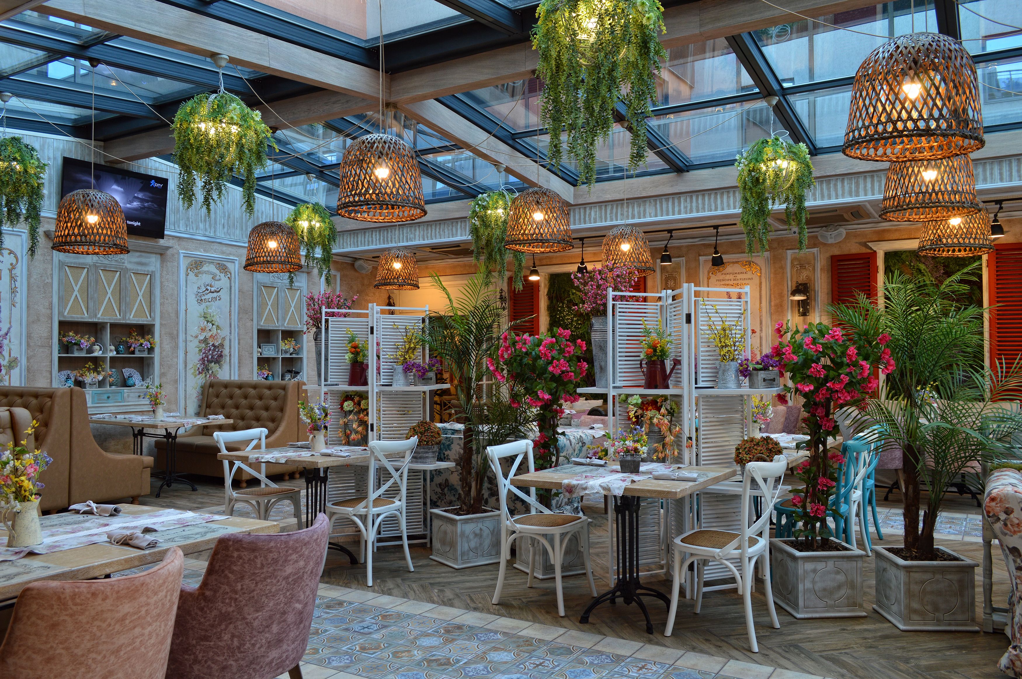 A spacious indoor area with multiple tables and chairs, hanging plants, and a glass ceiling.