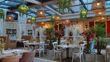 A spacious indoor area with multiple tables and chairs, hanging plants, and a glass ceiling.