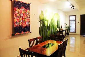 Un comedor con una mesa y sillas de madera, un tapiz floral en la pared y una planta en maceta con hojas verdes grandes.