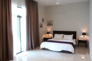 Habitación de hotel con una cama grande, dos mesitas de noche con lámparas, una ventana con cortinas y obras de arte en las paredes.