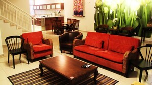 A living room with a sofa, chairs, a coffee table, and a kitchen in the background. - Balinese House (Malacca City)