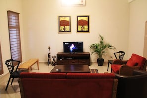 Una sala de estar con sofá, sillas, una mesita de centro, televisor, planta y obras de arte en la pared.