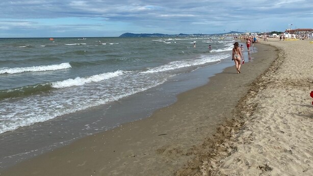 Una playa con olas, gente caminando y un cielo despejado.