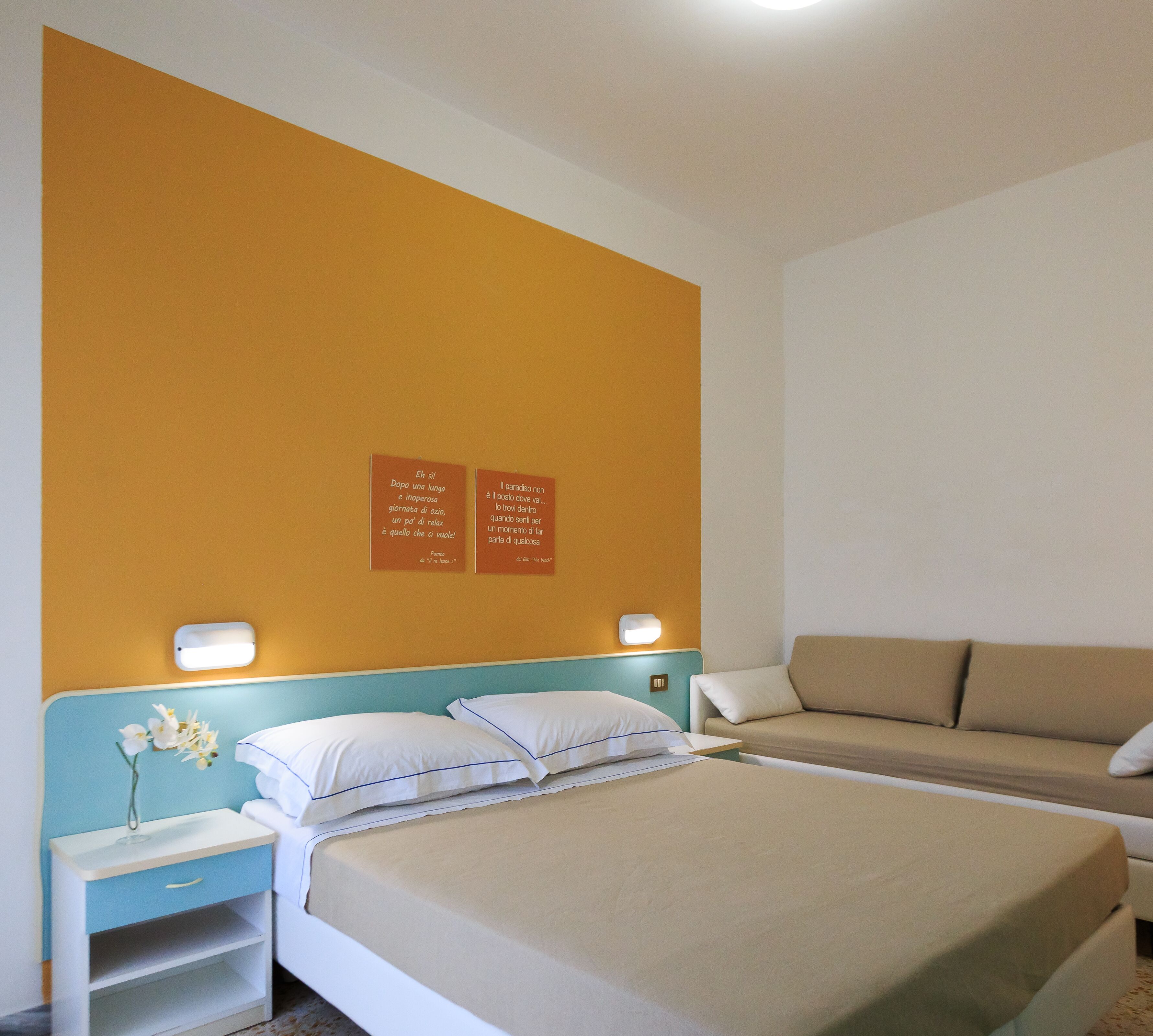 Una habitación de hotel con una cama, un sofá y dos lámparas fijadas a la pared.