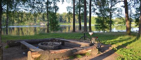 A campsite with a fire pit, a bicycle, and a lake in the background.