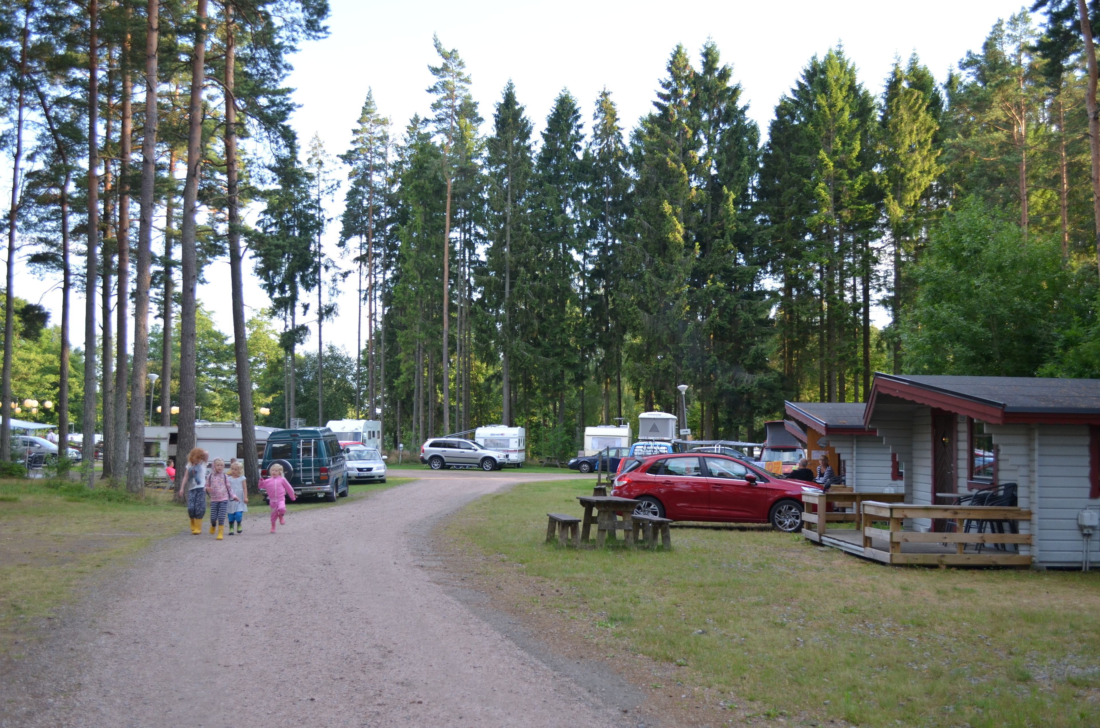 Un terrain de camping avec des camping-cars, une voiture rouge et une petite cabane.