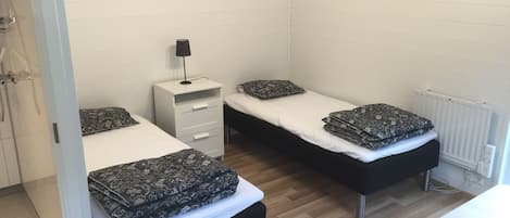 A room with two beds, a small desk, and a radiator.
