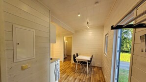 A narrow hallway with wooden walls and a wooden floor leading to a dining area with a table and chairs.