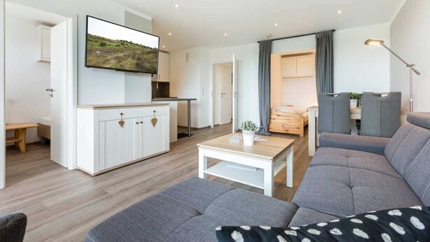 A modern living room with a grey sofa, a coffee table, and a flat-screen TV mounted on the wall. - Apartment 93 (ID 082), Germany (Sankt Peter-Ording)