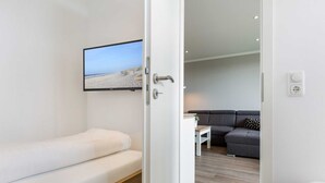 A modern room with a bed, a TV mounted on the wall, a sofa, and a small table. - Apartment 93 (ID 082), Germany (Sankt Peter-Ording)