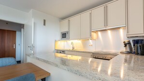 Uma cozinha moderna com armários brancos, bancada de granito e micro-ondas embutido.