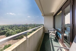 A balcony with a view of a cityscape, a table with chairs, and a window with a view of the greenery below.
