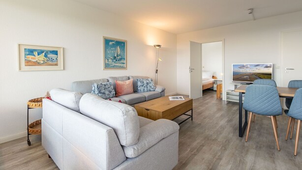 Uma sala de estar moderna com um sofá cinzento, uma mesa de centro de madeira e uma área de jantar com cadeiras azuis.