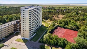 A high-rise hotel with multiple floors, surrounded by lush greenery and a tennis court. - Apartment 193 (ID 290) - House Atlantic (Sankt Peter-Ording)