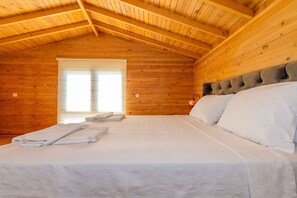 A wooden cabin room with a bed, a window with blinds, and a ceiling with wooden beams. - Anatolian Apartments (Fethiye)