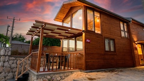 A wooden cabin with a stone foundation, a wooden deck, and a large window. - Anatolian Apartments (Fethiye)