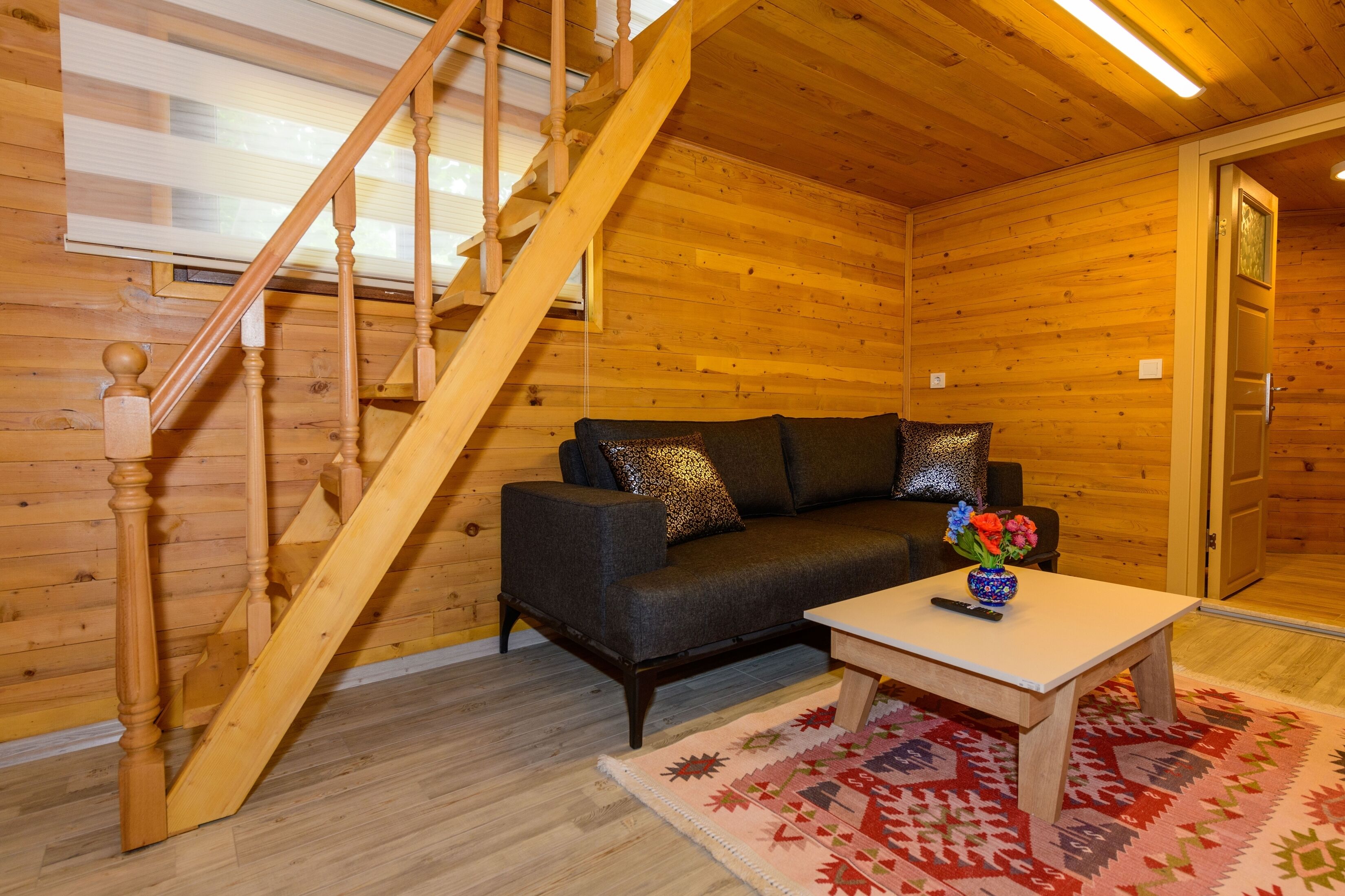 Un interior de madera con una escalera, un sofá, una mesa y una alfombra.