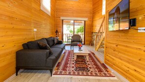 A cozy wooden cabin interior with a sofa, armchair, and a flat-screen TV mounted on the wall. - Anatolian Apartments (Fethiye)