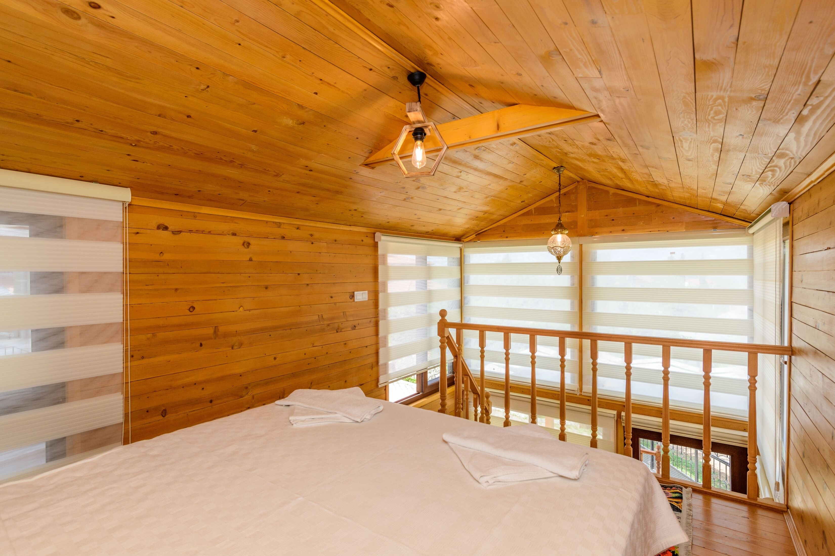 Een slaapkamer in een houten hutje met een bed, een plafondventilator en uitzicht door het raam.
