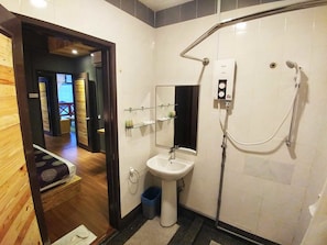 Een moderne badkamer met douche, wastafel en spiegel. Er ligt een houten vloer en er staat een klein prullenbakje.
