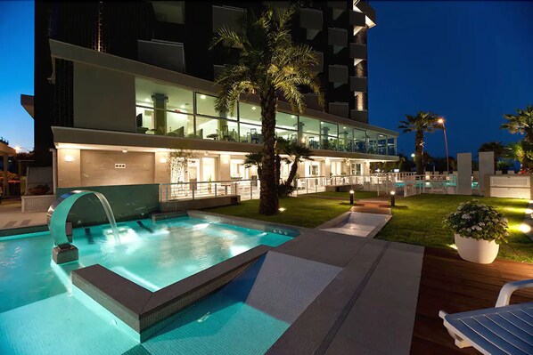 Ein modernes Hotel mit Schwimmbad, Palmen und einem gut beleuchteten Außenbereich.
