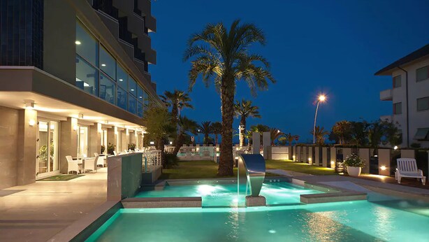 Una piscina con fuente, rodeada de palmeras y edificios modernos.