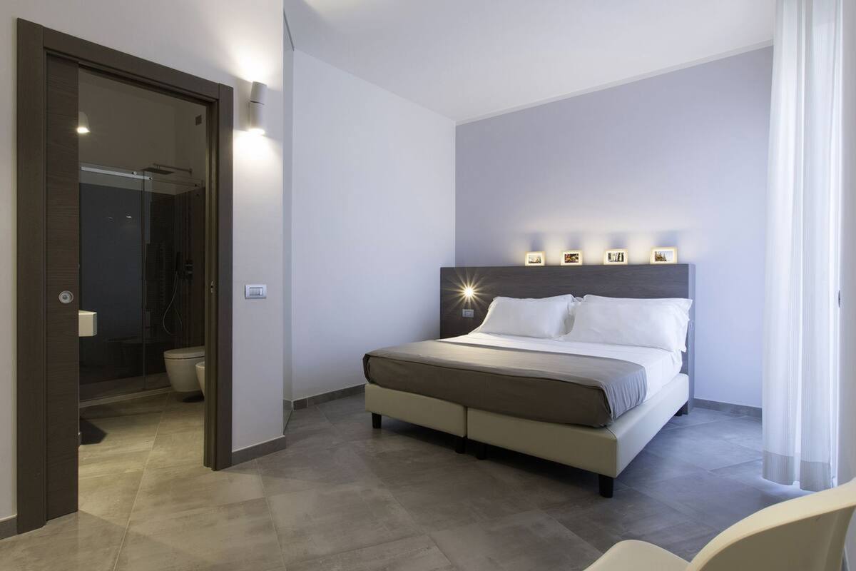 A modern hotel room with a large bed, a bedside table, and a wall-mounted light fixture.