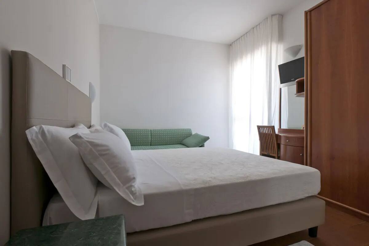 A bedroom with a bed, a wooden wardrobe, a desk, and a chair.