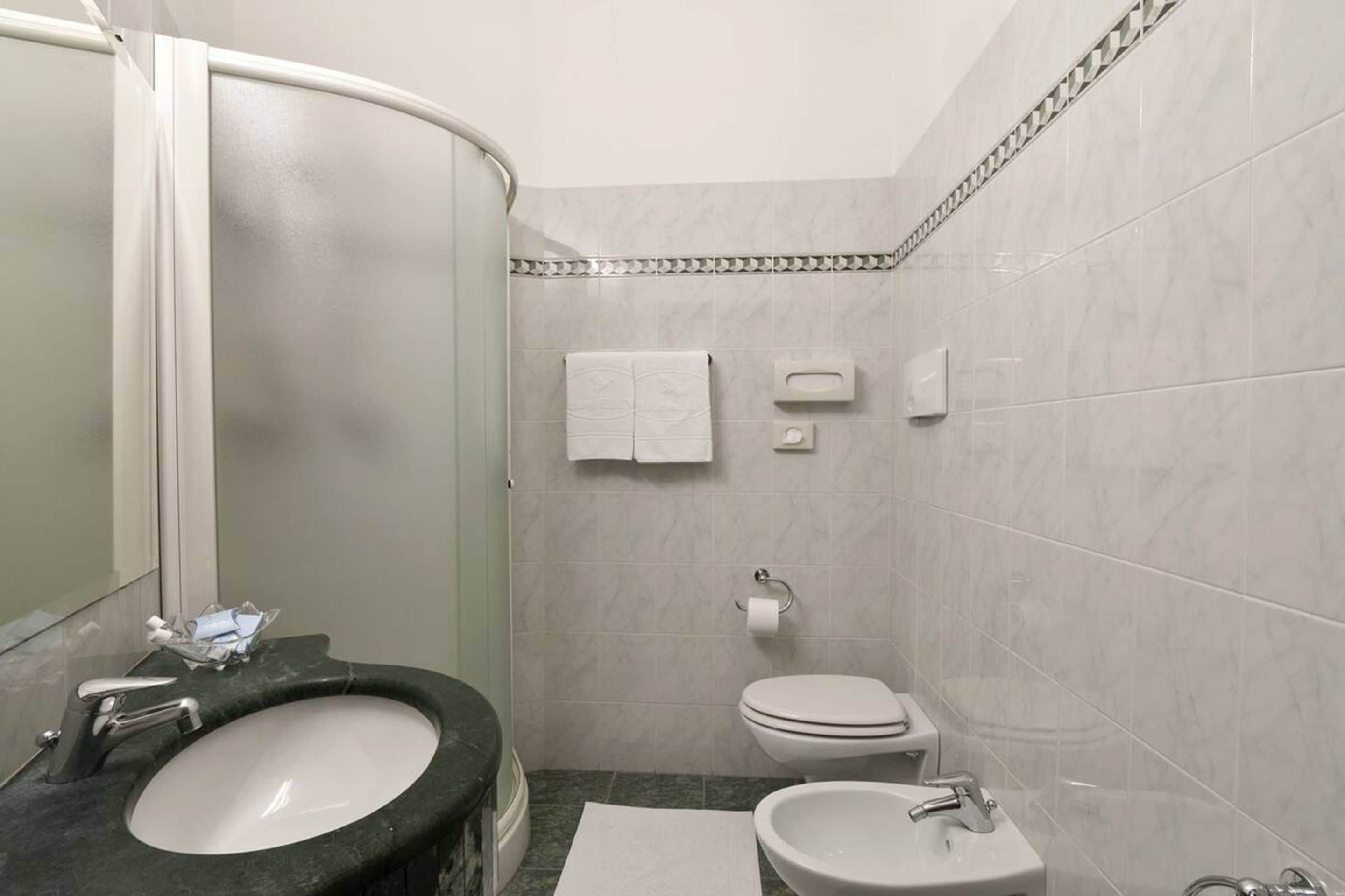 A bathroom with a curved shower, a sink, a toilet, and a mirror.