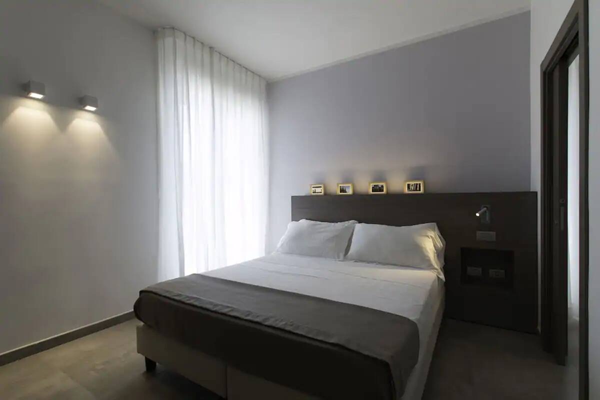 A modern hotel room with a large bed, a nightstand, and a wall-mounted light fixture.
