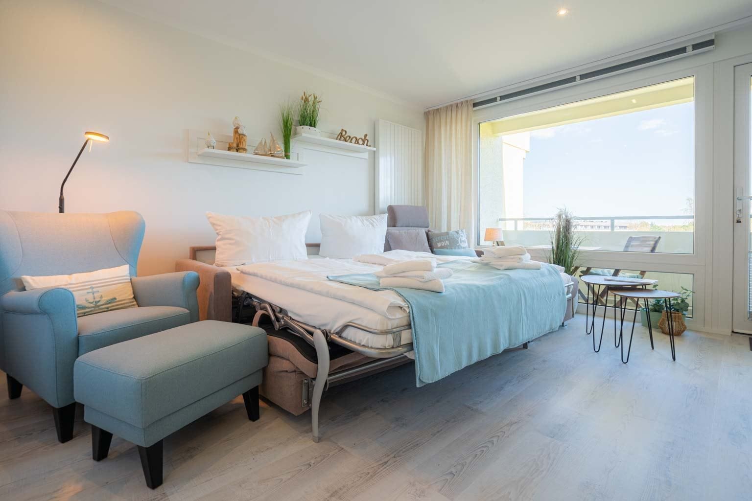 Een moderne hotelkamer met een bed, een stoel, een klein tafeltje en een balkon met uitzicht.