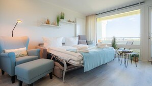 A modern hotel room with a bed, a chair, a small table, and a balcony with a view. - Apartment 254 Little time-out (ID 139) (Sankt Peter-Ording)