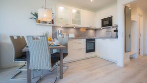 A modern kitchen with white cabinets, a built-in oven, and a microwave. There is a dining area with a table and chairs. - Apartment 254 Little time-out (ID 139) (Sankt Peter-Ording)