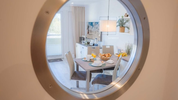 A dining area with a round mirror reflecting a kitchen and dining space. - Apartment 254 Little time-out (ID 139) (Sankt Peter-Ording)