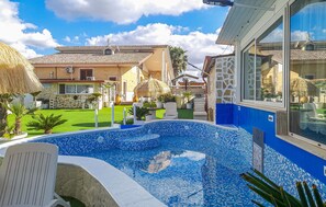 A swimming pool with blue mosaic tiles, surrounded by a well-maintained lawn and a stone wall.