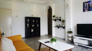 En moderne stue med sofa, sofabord, tv-møbel, en sort reol og en lysekrone.