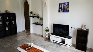 En moderne stue med et fladskærms-tv, et hvidt tv-møbel, et sort reolsystem og en dekorativ plante.