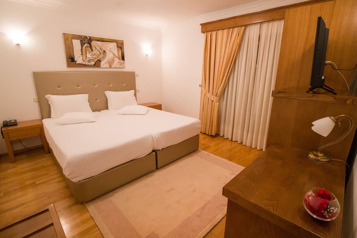 Un dormitorio ordenado con una cama, mesitas de noche, un escritorio y un televisor.