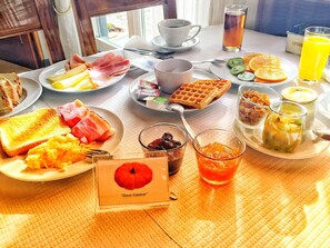 Una mesa de desayuno con platos de comida, un gofre, un vaso de jugo y un cartel con una manzana roja.