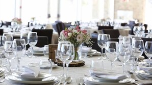 Un comedor con mesas dispuestas para una comida, incluyendo platos, cubiertos y copas de vino.