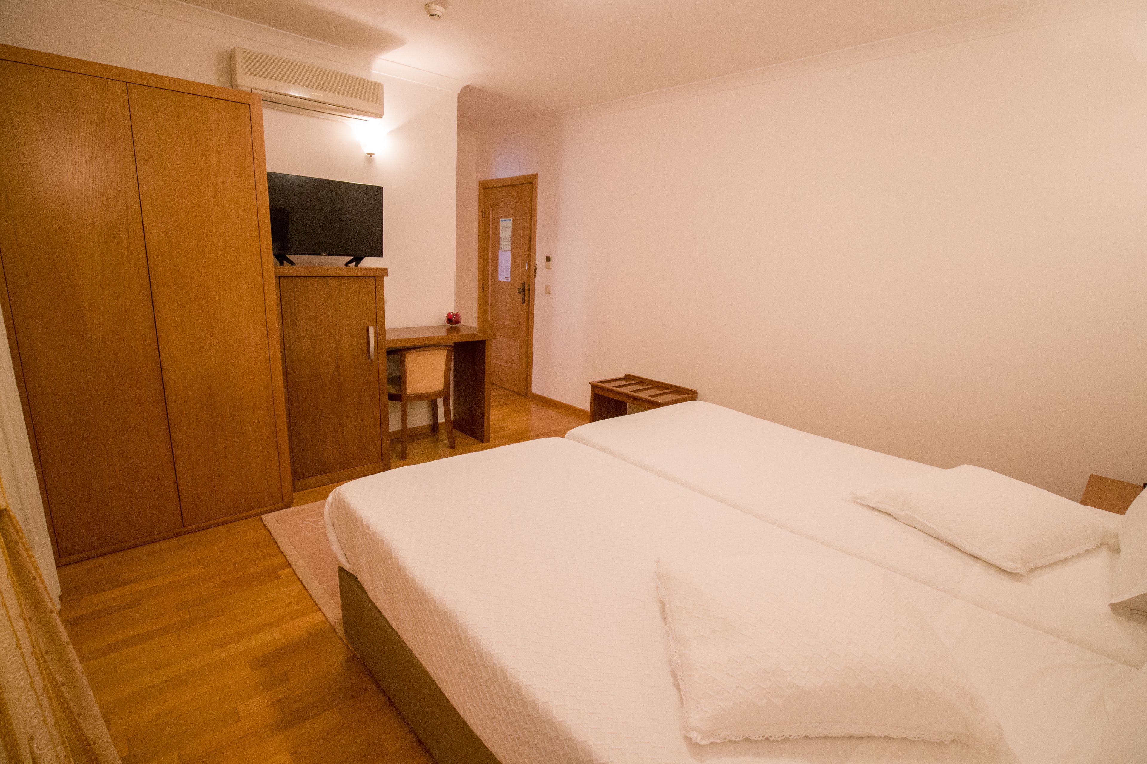 A bedroom with a bed, wooden wardrobe, desk, chair, and a television.