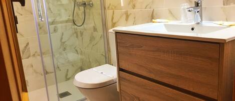 Un baño con inodoro, tocador de madera con lavamanos y cabina de ducha de vidrio.