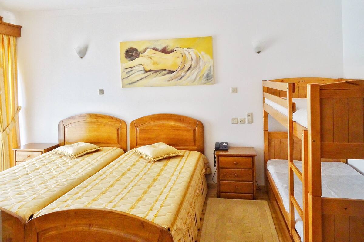 Un dormitorio con dos camas de madera, una mesita de noche, una cama litera y un cuadro en la pared.