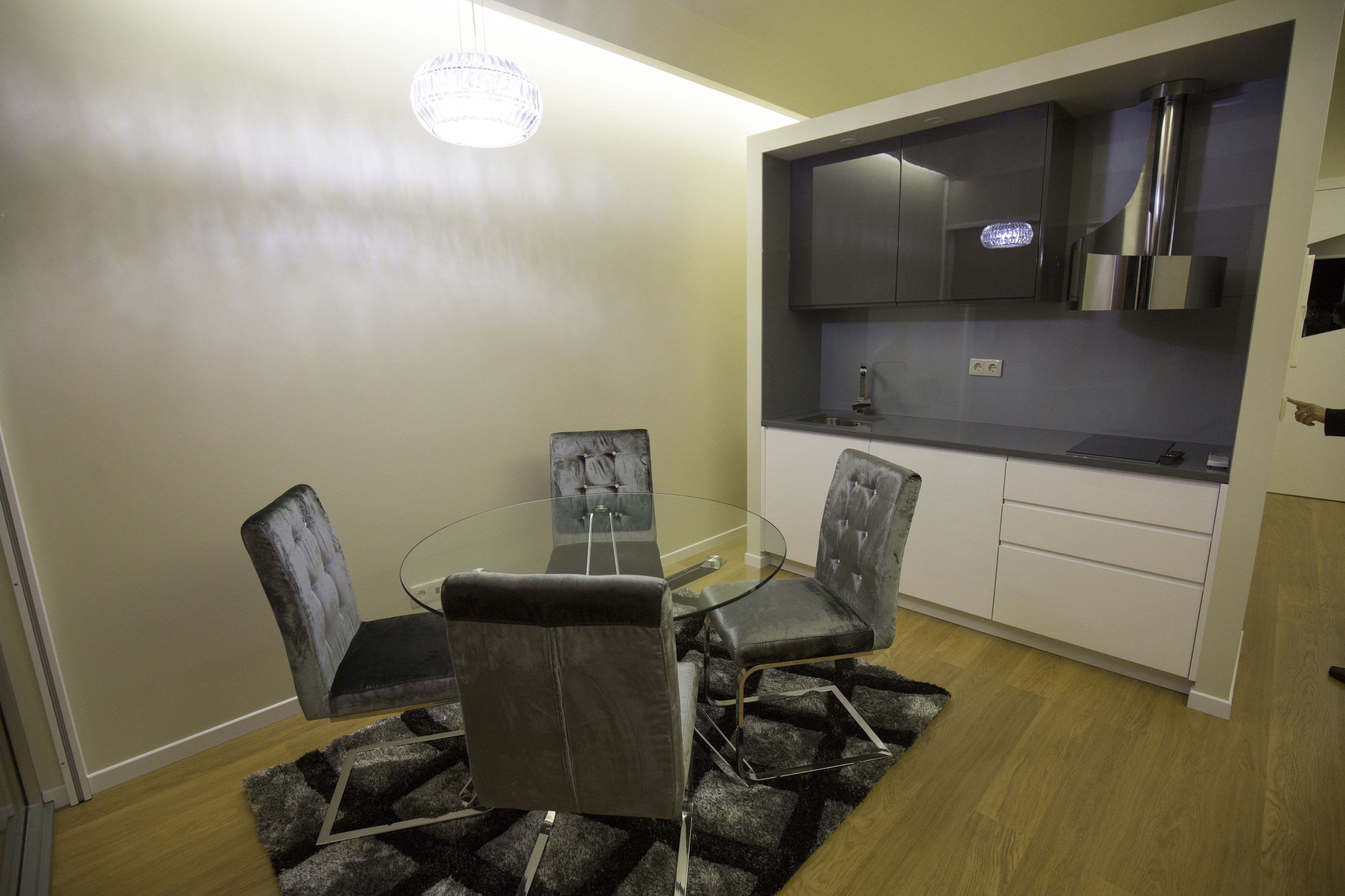 A compact kitchen with a built-in oven, a dining area with a glass table and four chairs, and a modern pendant light.