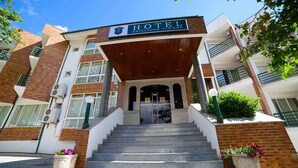 Entrada de un hotel con un letrero que dice "HOTEL ESTALAGEM TURISMO", un conjunto de escaleras que conducen a la entrada y dos macetas grandes con flores.