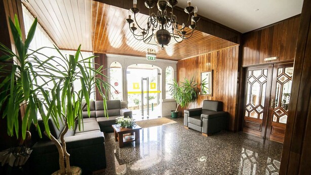 Un vestíbulo con piso de granito pulido, paneles de madera y una araña. Hay dos sofás y una mesa de centro con un arreglo floral.