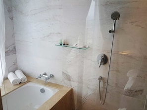A bathroom with a bathtub, a shower, and a glass shelf with toiletries.