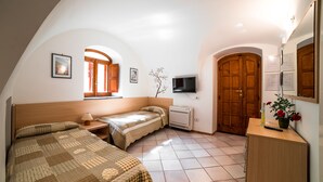 A bedroom with two beds, a TV, a wooden wardrobe, and a window with curtains. - Il Roseto (Ravello)